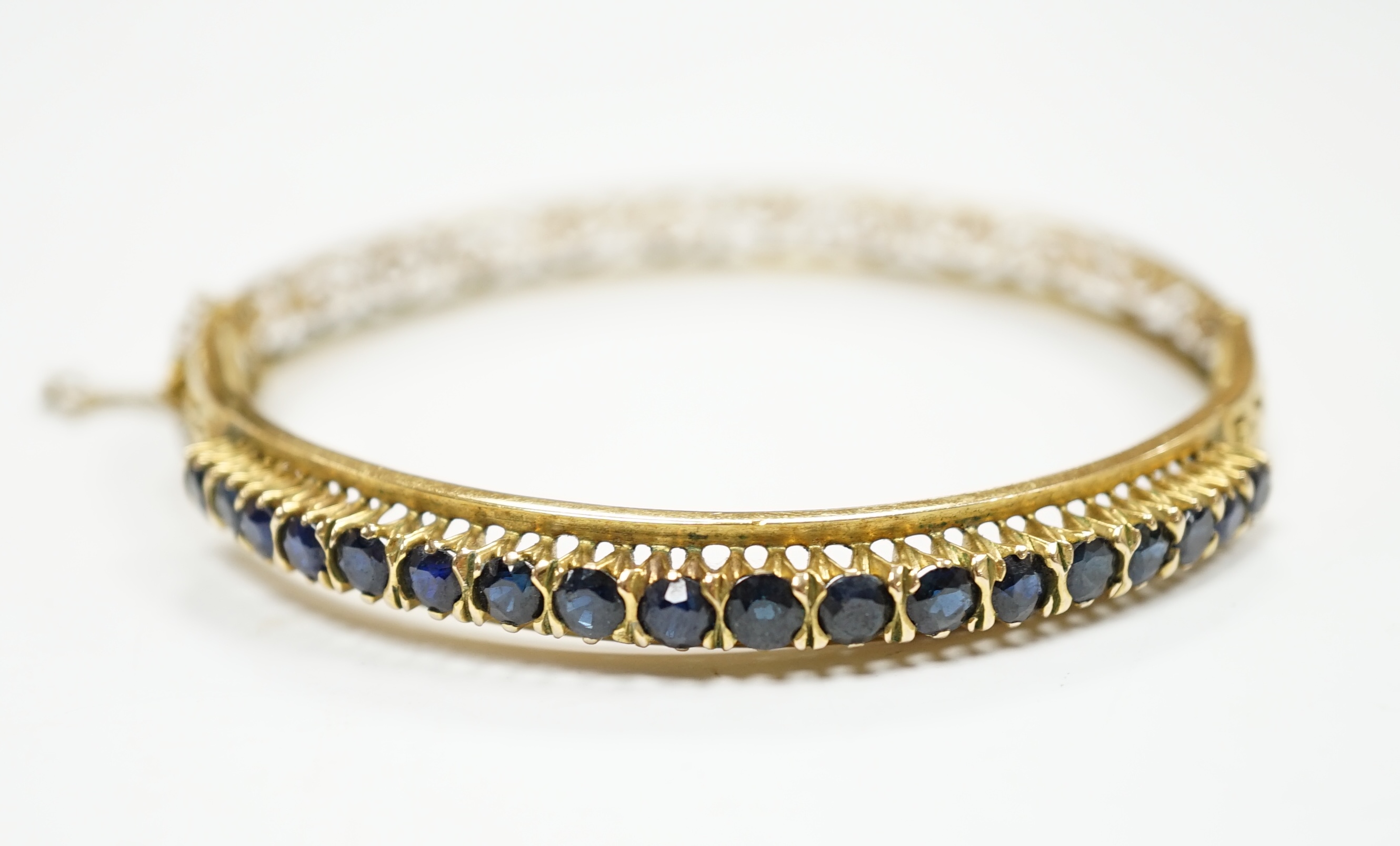A pierced yellow metal and eighteen stone sapphire set hinged bangle, interior diameter 58mm, gross weight 14.1 grams.